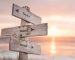 Wooden street sign reading mind, body, and soul with sunset and water in the background, symbolizing a spiritual journey.
