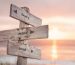 Wooden street sign reading mind, body, and soul with sunset and water in the background, symbolizing a spiritual journey.